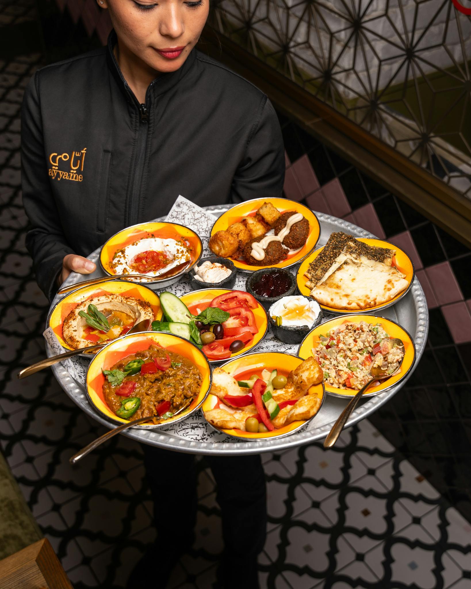 Waitress carrying a vibrant assortment of Mediterranean dishes in a restaurant setting.